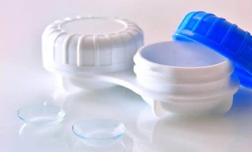 Open contact lens case with blue lid and two clear contact lenses beside it