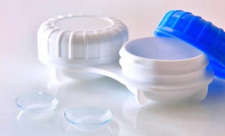 Open contact lens case with blue lid and two clear contact lenses beside it
